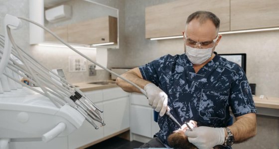 Afbeelding van een tandarts bezig met apparatuur bij patiënt met baard.