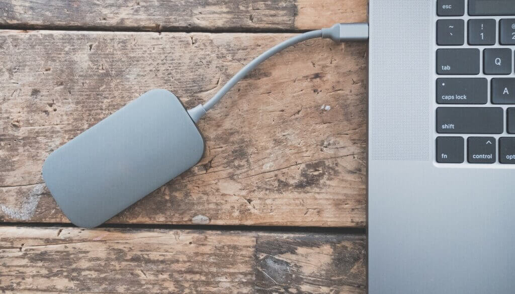 Een laptop aangesloten op een USB-kabel voor back-up op een houten tafel.