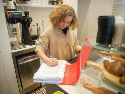 Vrouw met krullen vult informatie in dikke map met papieren